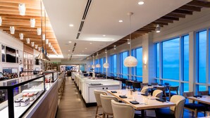 A modern restaurant with a long counter, multiple dining tables, and large windows offering a view of the sea. - Lido Beach Resort (Sarasota)