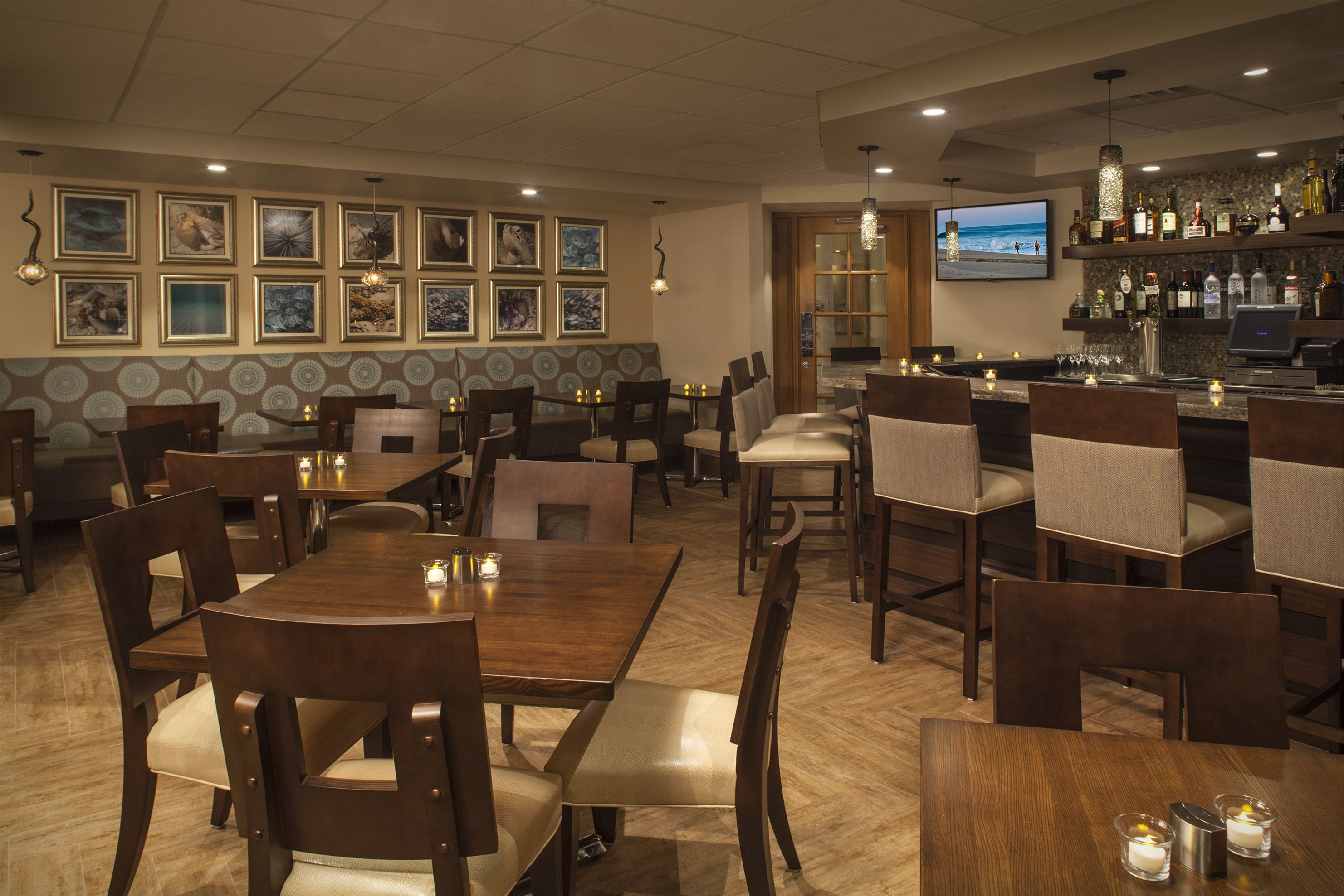 A restaurant with wooden tables and chairs, a bar area with a TV, and framed artwork on the walls.