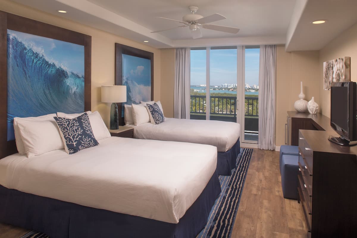 A hotel room with two beds, a ceiling fan, a TV, and a balcony with a view.