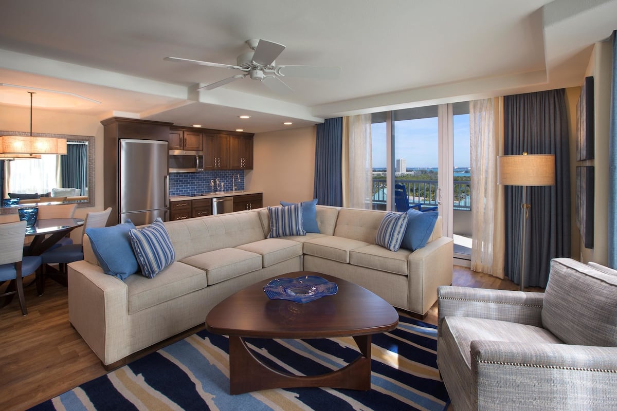 A modern hotel room with a living area, kitchenette, and a balcony with a city view.