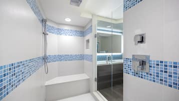 A modern bathroom with a glass shower enclosure, a white bathtub, and blue mosaic tiles on the walls.