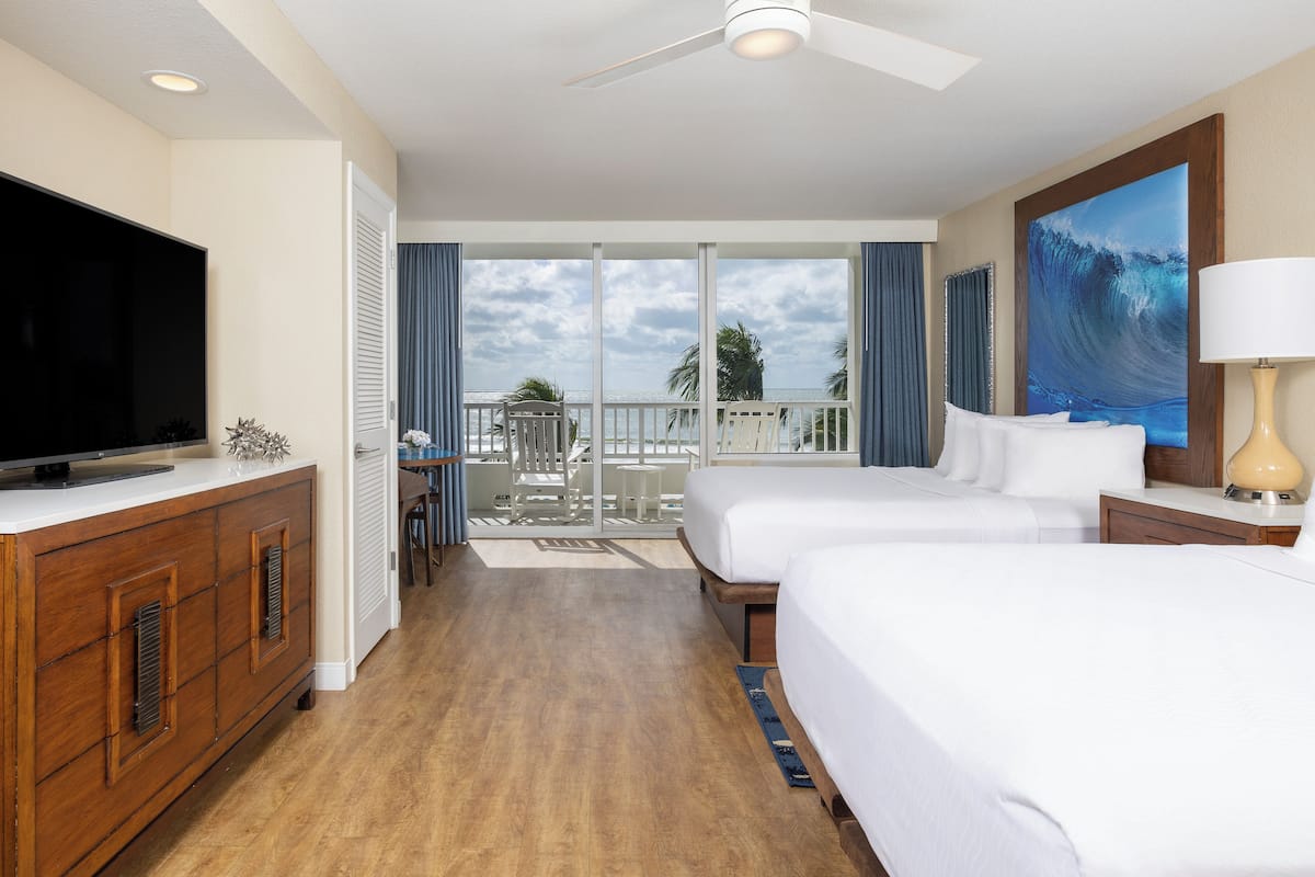 A hotel room with a balcony, a television, two beds, and a painting.