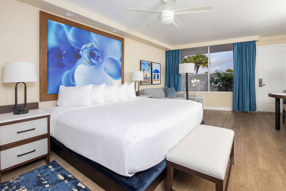 A hotel room with a large bed, bedside tables, a desk, and a balcony with curtains.