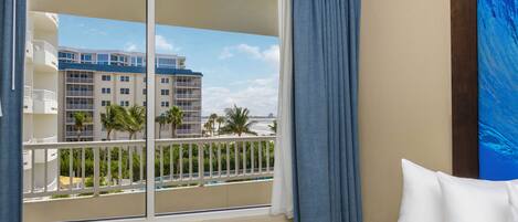 Une chambre d’hôtel avec une grande fenêtre, une vue sur un immeuble doté de balcons et un tableau accroché au mur.