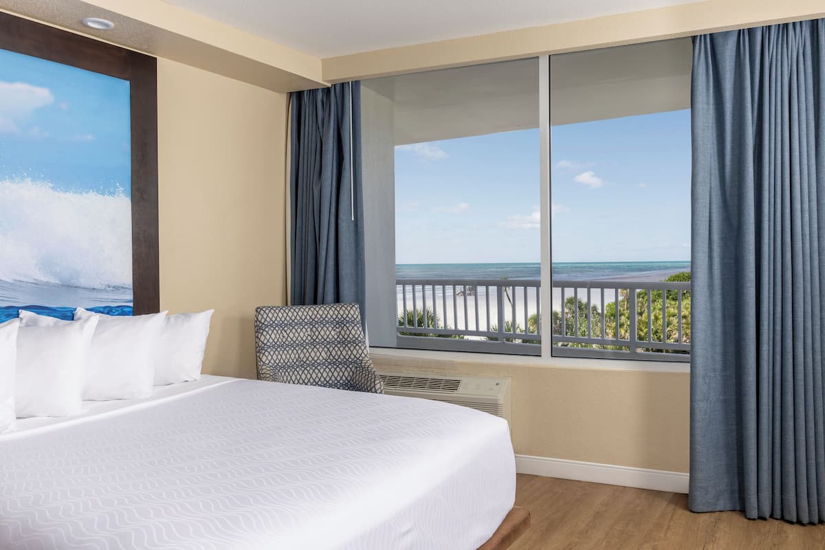 A hotel room with a large bed, a view of the ocean, and a balcony with curtains.