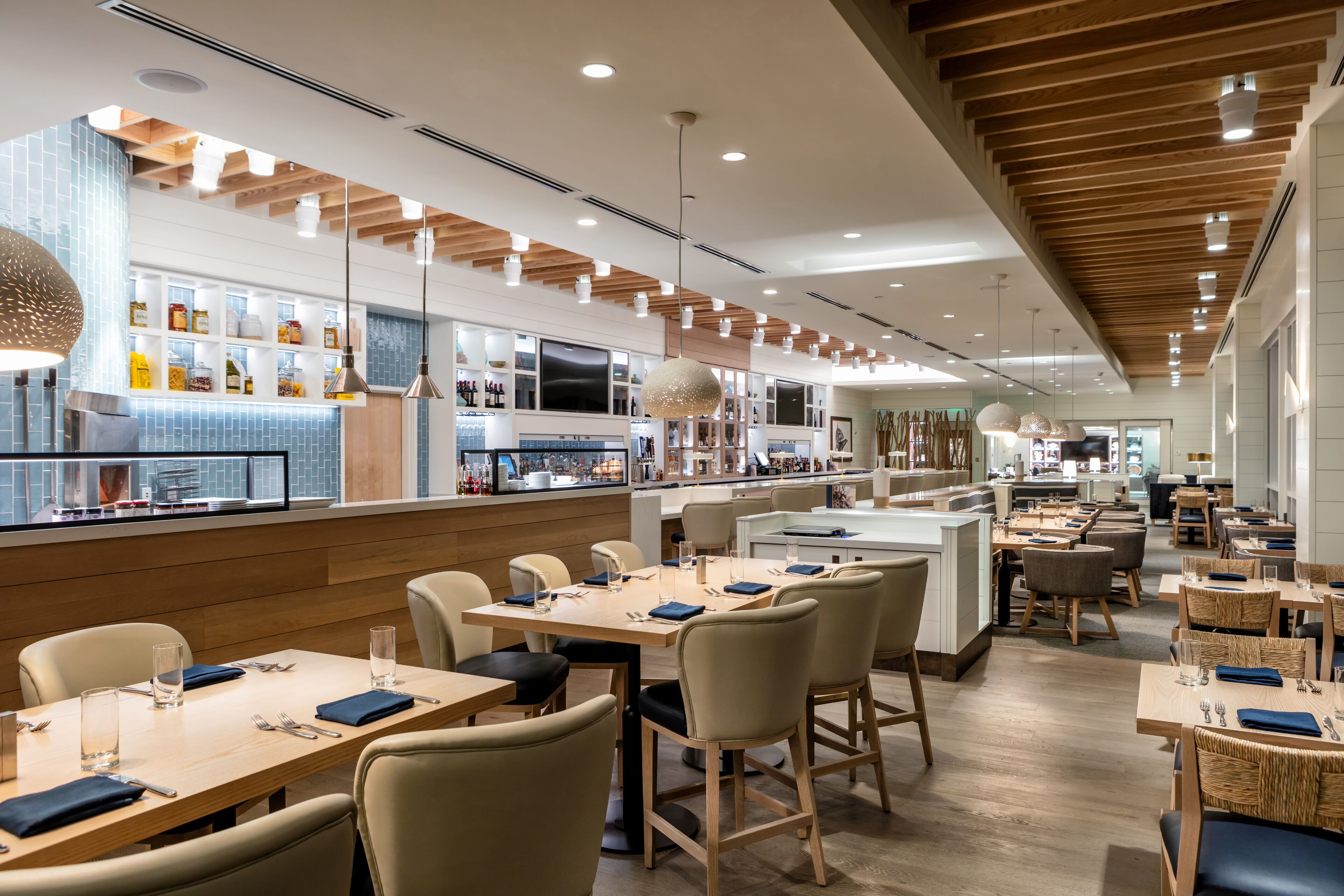 Ein modernes Restaurant mit Holzbalkendecke, einer Bar mit Flaschen und Tischen mit Stühlen.