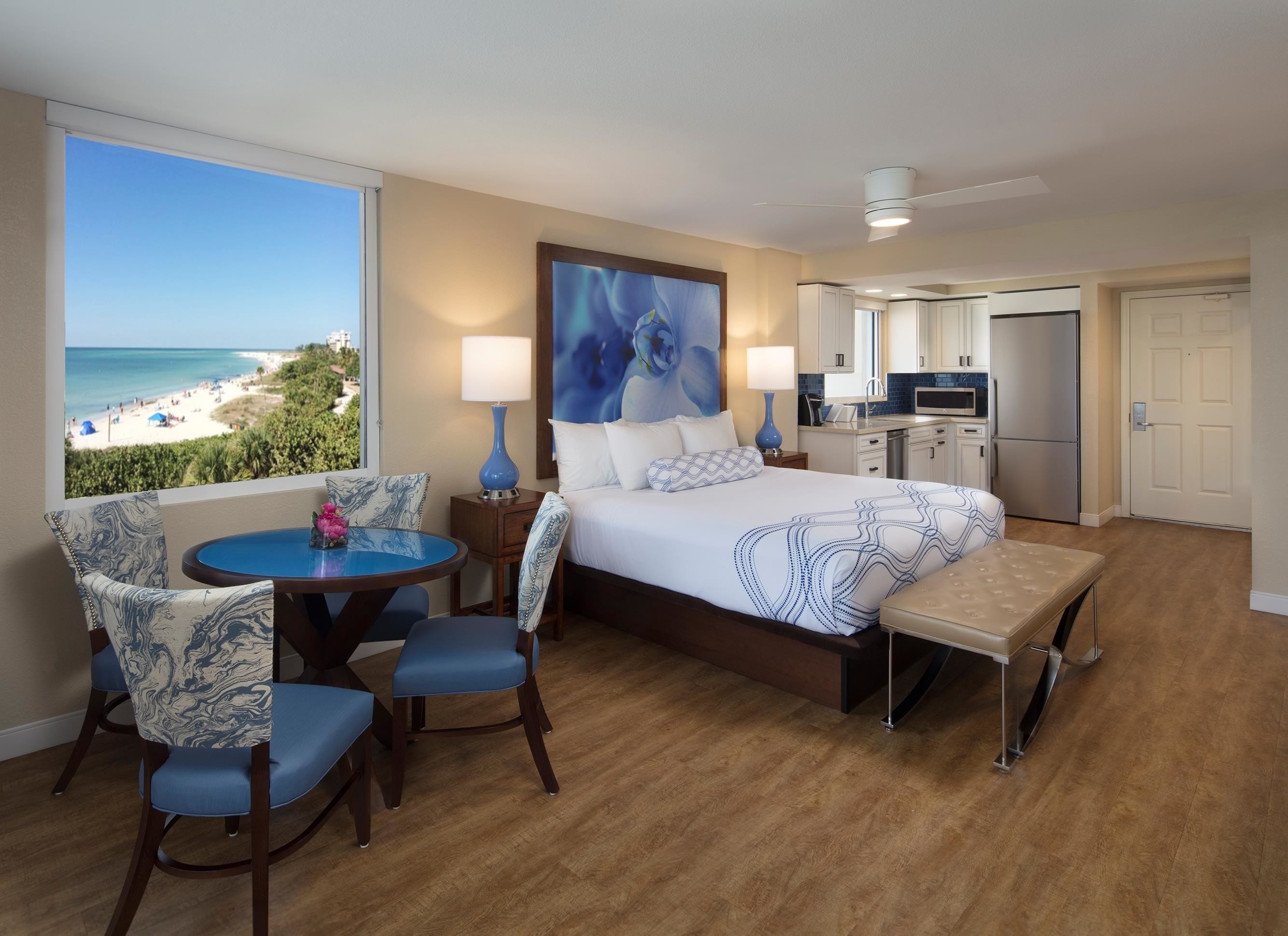 Ein Hotelzimmer mit einem großen Bett, einem Schreibtisch mit Stuhl, Blick auf den Strand und einer Küchenzeile.