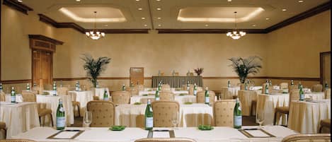 A banquet hall with multiple round tables, each set with chairs, wine glasses, and bottles of water.