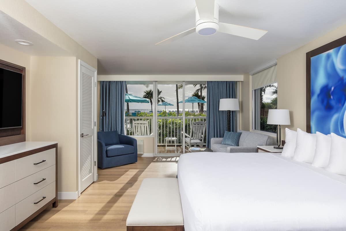 A hotel room with a bed, a desk, a chair, a TV, and a balcony with umbrellas.