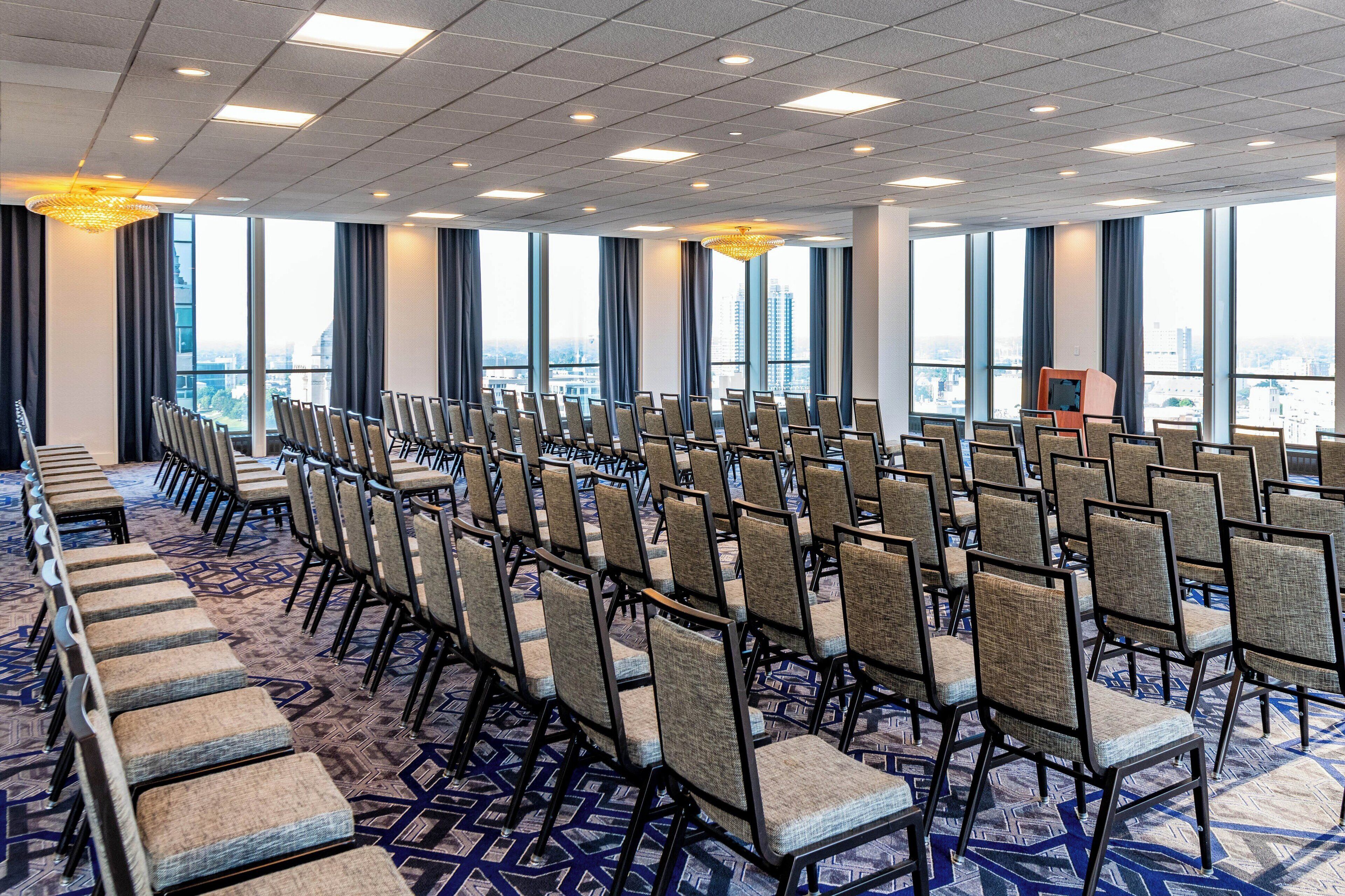 A conference room with rows of chairs, large windows, and a city view.