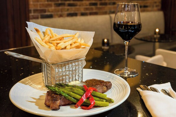 Un plato con bistec, espárragos y papas fritas sobre una mesa con una copa de vino.