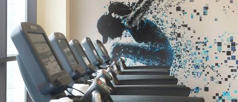 Une rangée d’appareils de musculation, avec une fresque d’art numérique en arrière-plan.