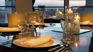 A dining table set for a meal with candles, glasses, and cutlery, overlooking a cityscape. - Sheraton Indianapolis City Centre Hotel (Indianapolis)