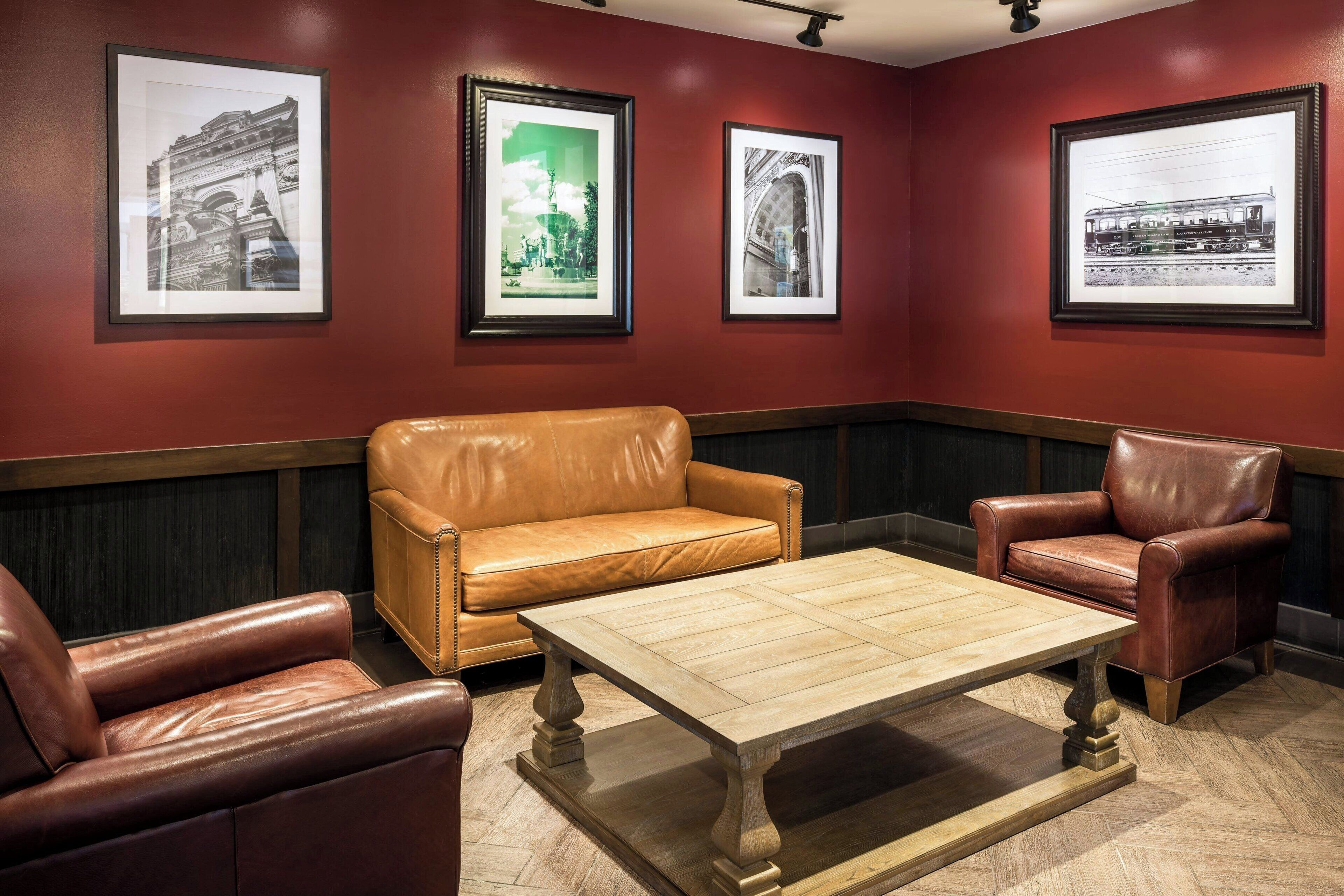 A room with a brown leather sofa, a matching armchair, and a wooden coffee table. There are framed pictures on the wall.