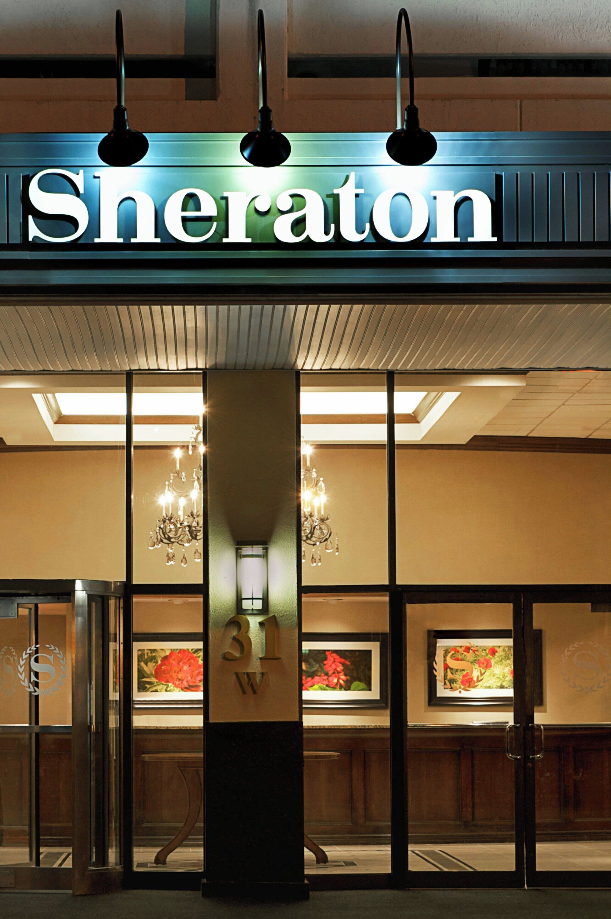 L’entrée d’un hôtel, avec une enseigne indiquant « Sheraton » et un grand pilier portant le numéro « 31 » et la lettre « W », qui indiquent le numéro de la chambre.