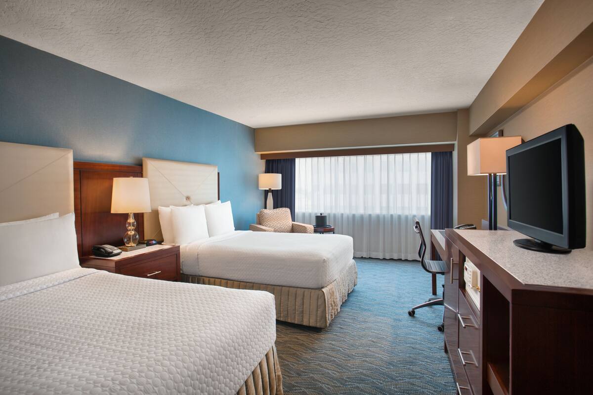 A hotel room with two beds, a desk with a television, and a window with curtains.