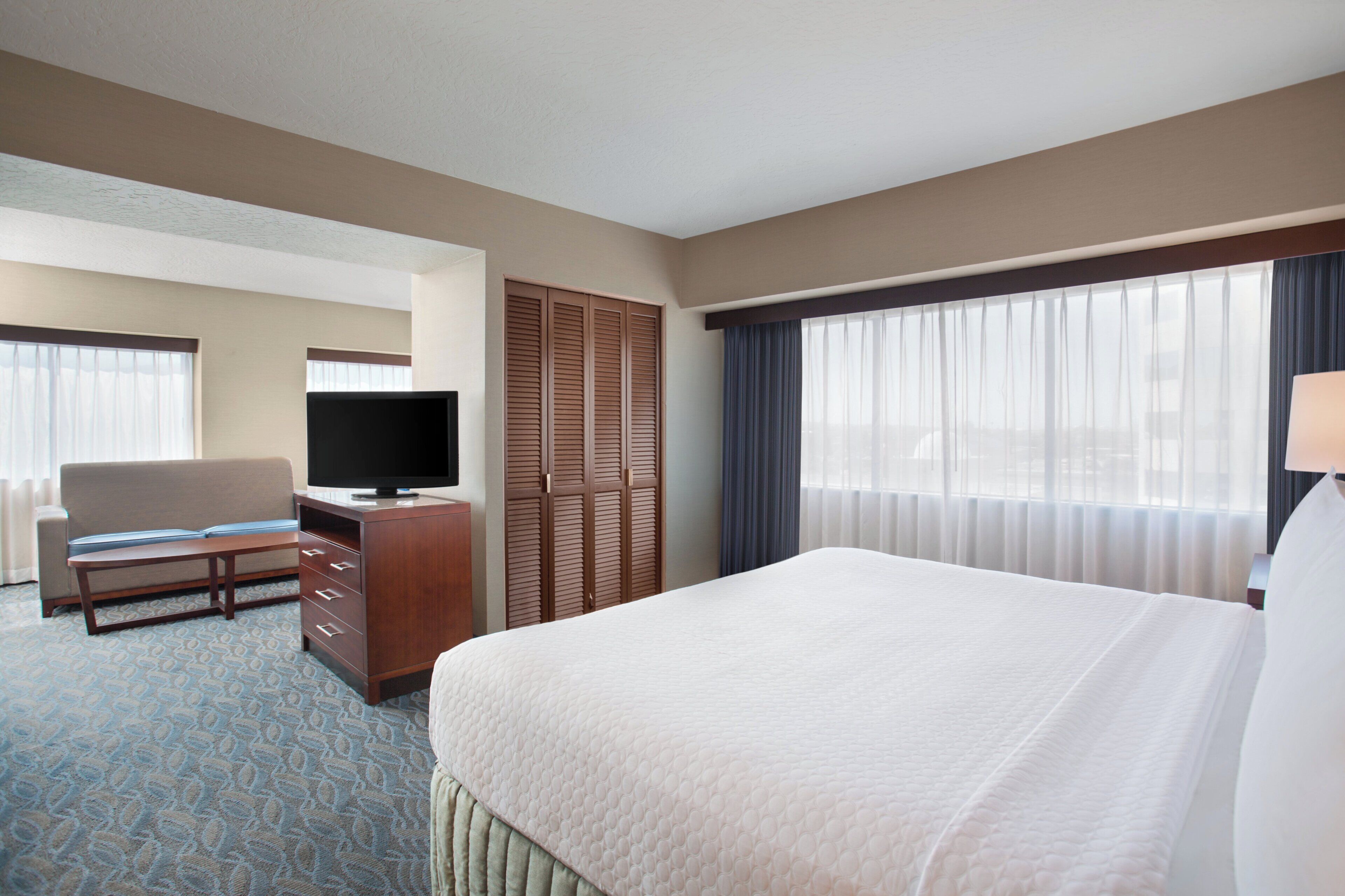 A hotel room with a bed, a television, a desk, a chair, and a wardrobe.