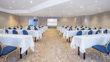 A conference room with rows of tables, chairs, and a projection screen in the background.