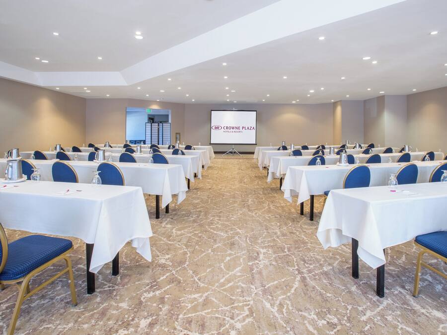 A conference room with rows of tables, chairs, and a projection screen in the background.