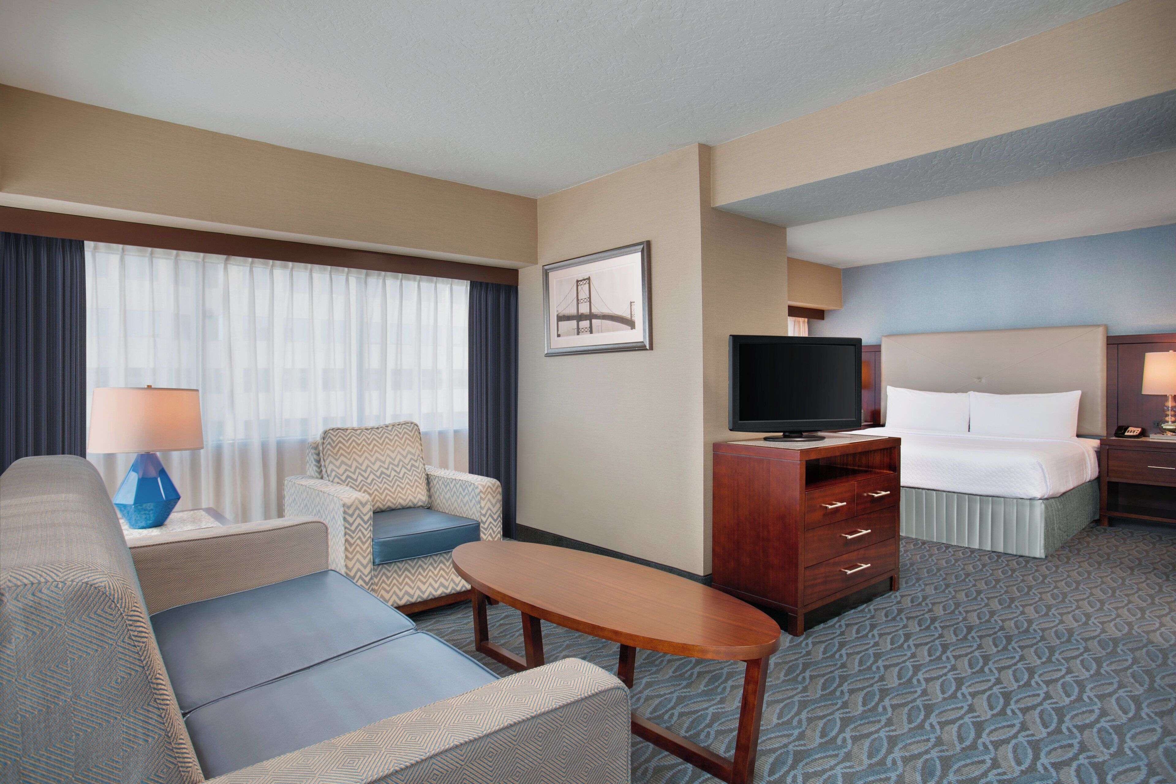 Una habitación de hotel con una cama, televisión, escritorio con lámpara, sofá y una silla.