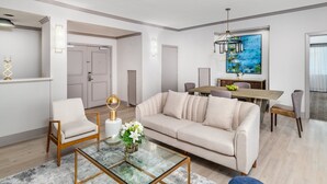 A modern living room with a sofa, armchair, glass coffee table, and a dining area with a table and chairs. - Crowne Plaza Los Angeles Harbor Hotel by IHG (San Pedro)