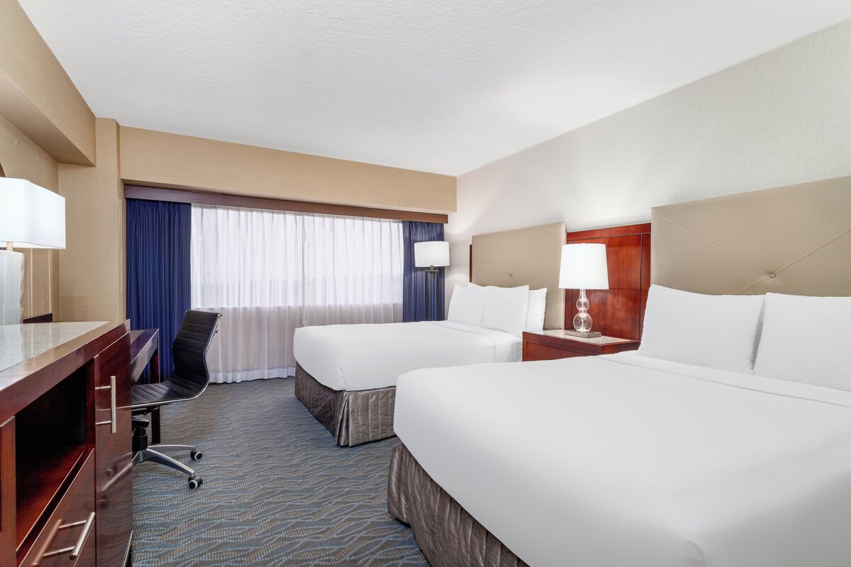 A hotel room with two beds, a desk, a chair, and a window with curtains.