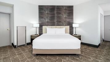 Habitación de hotel con una cama grande, dos mesitas de noche con lámparas, cabecero y suelo alfombrado.