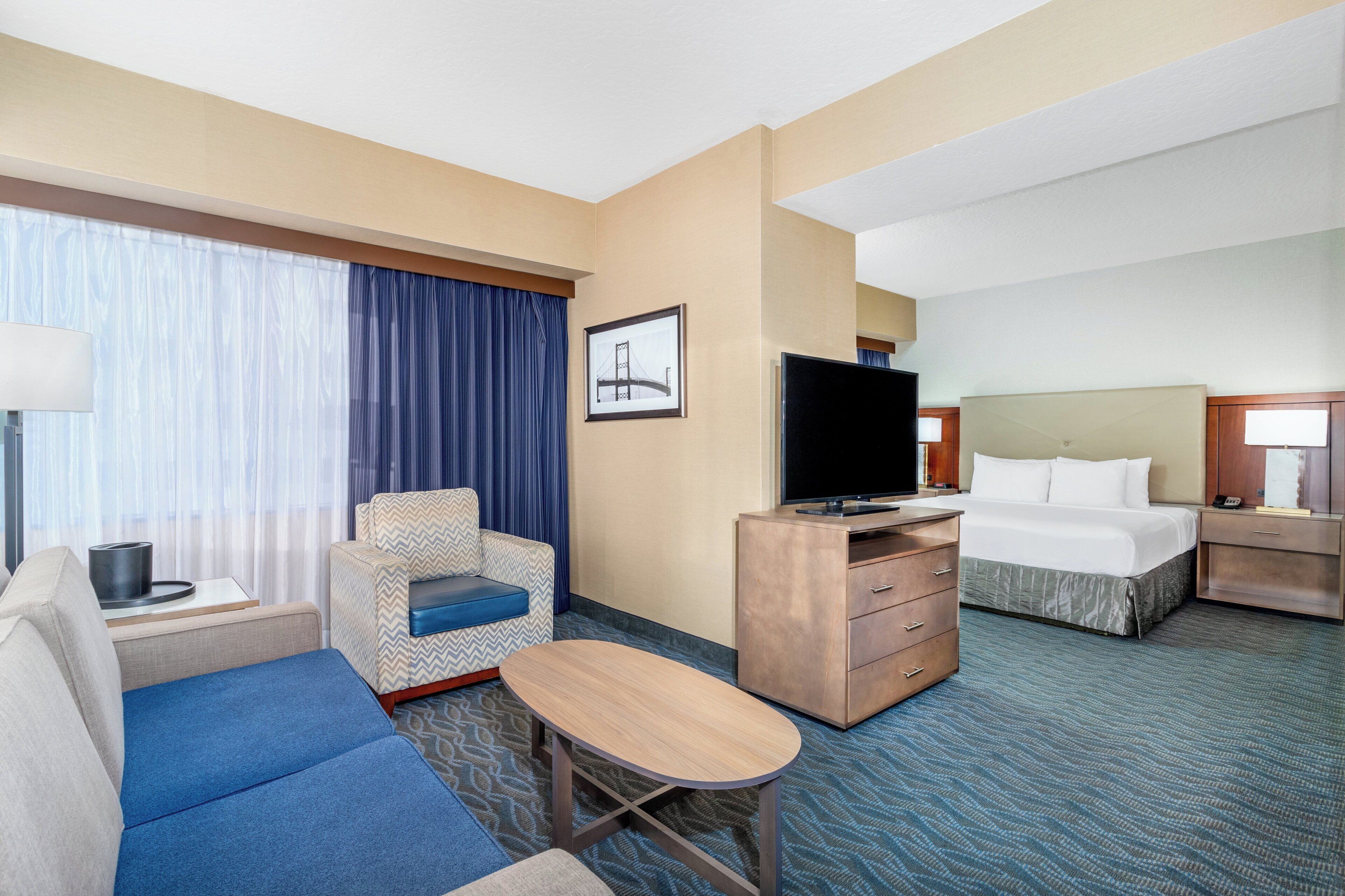 A hotel room with a sofa, a small table, a TV, a bed, and a nightstand.