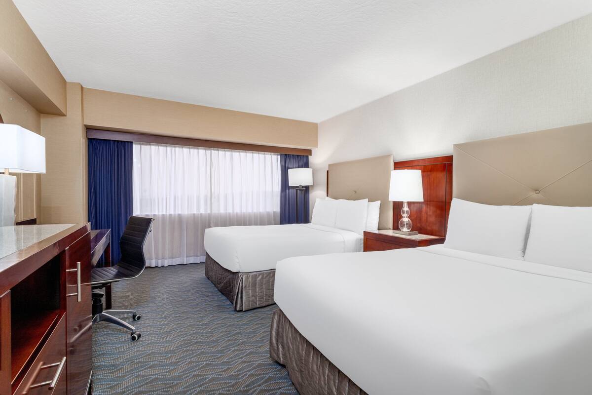 A hotel room with two beds, a desk, a chair, and a window with curtains.