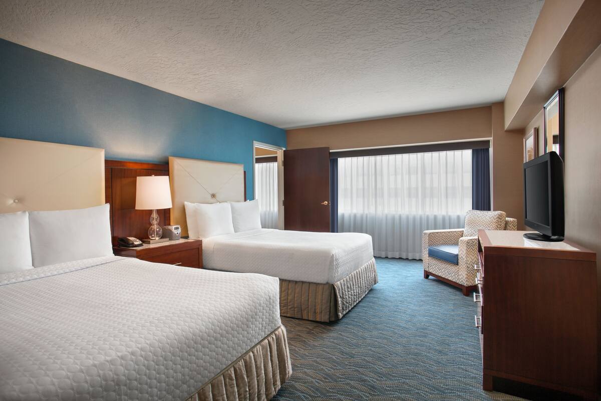 A hotel room with two beds, a desk with a lamp, a television, and a chair.