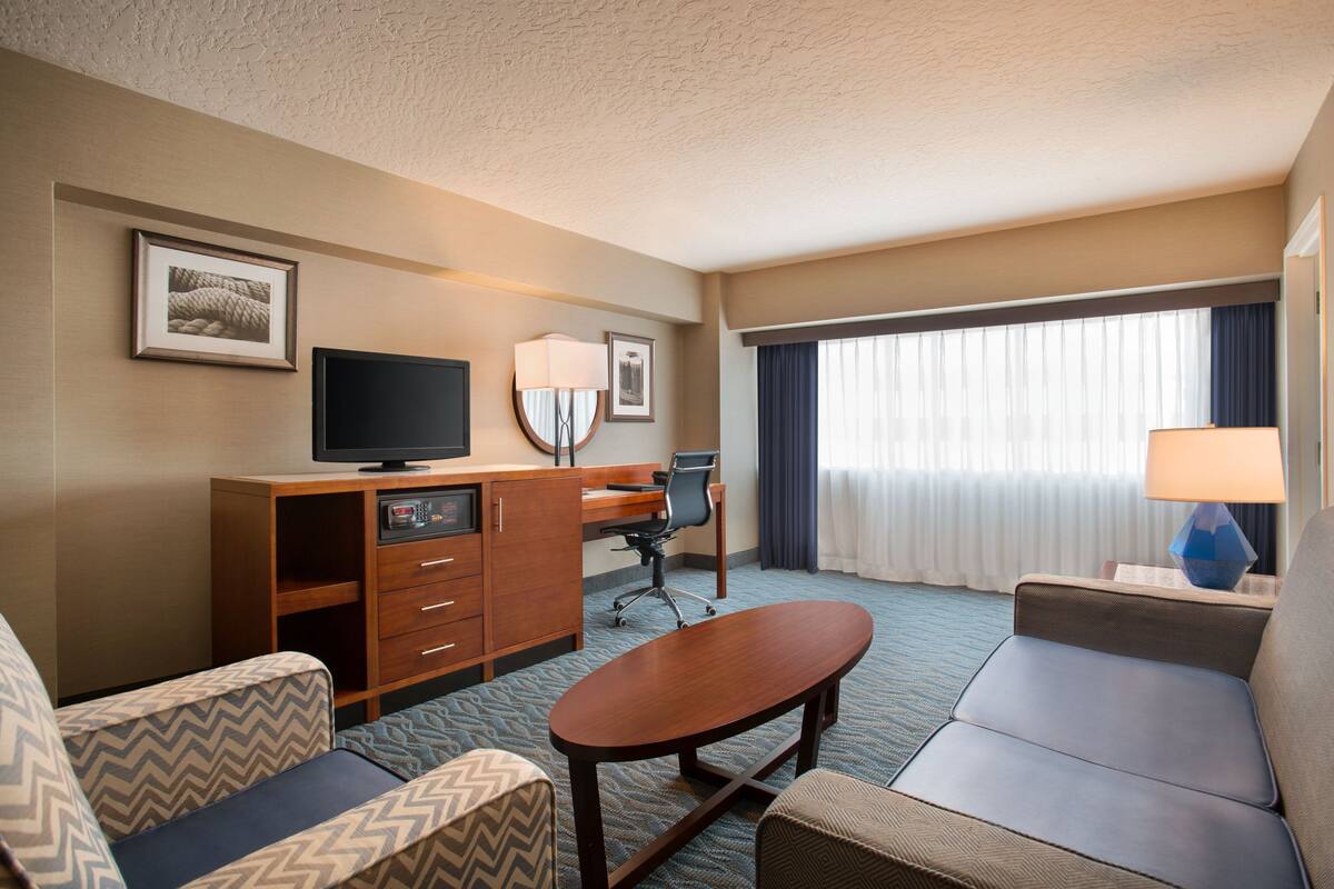 A hotel room with a sofa, a desk with a computer, a television, and a window with curtains.