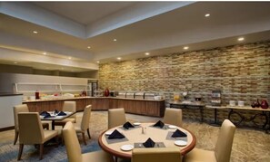 Un comedor moderno de hotel con pared de piedra, un mostrador de buffet y mesas redondas dispuestas para comer.