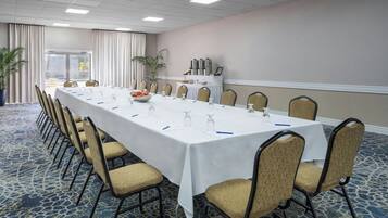 Un salón de conferencias con una larga mesa, sillas y un mantel blanco.