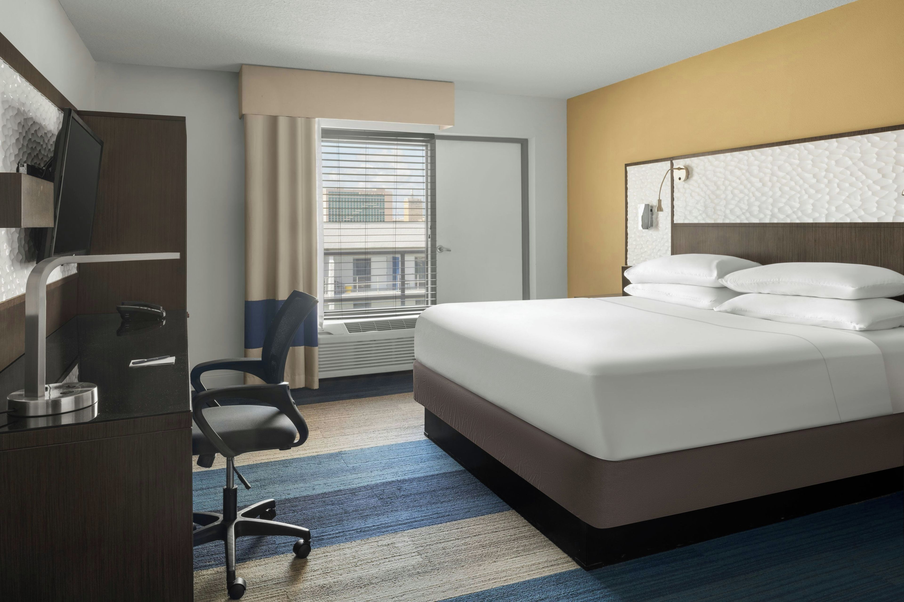 A hotel room with a bed, a desk, a chair, a television, and a window with blinds.