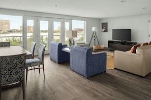 A modern living room with a dining area, a sofa, a TV, and a balcony with city views.