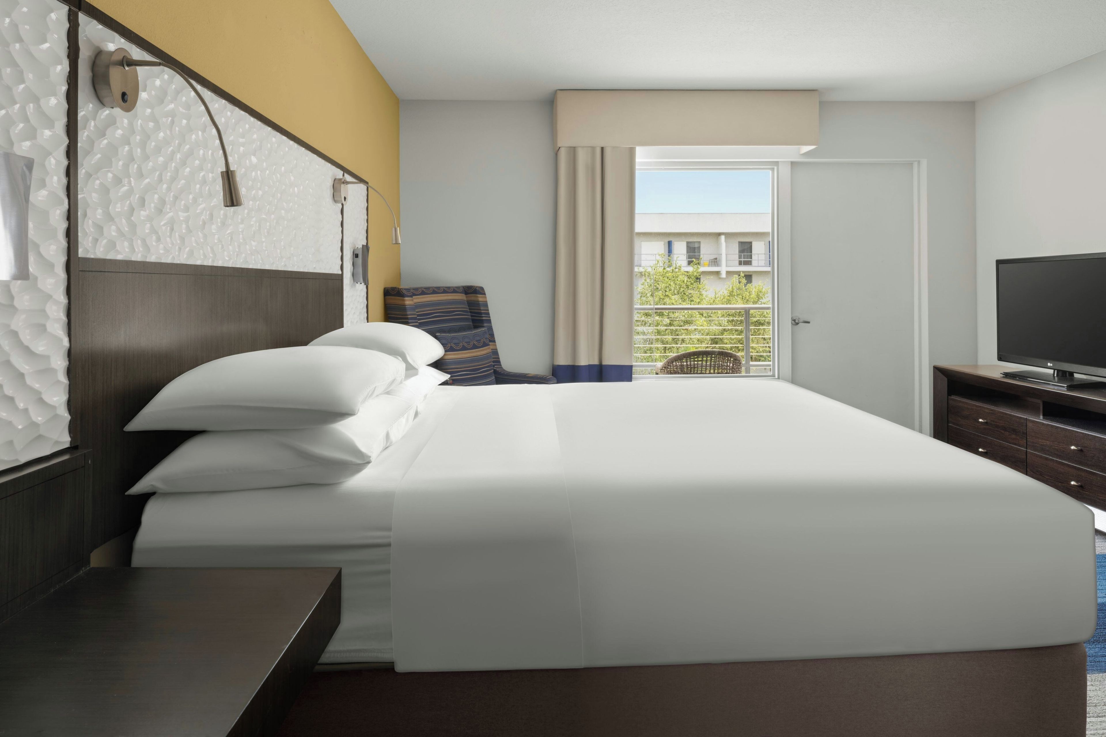 Ein Hotelzimmer mit einem großen Bett, einem Flachbildfernseher, einem Schreibtisch und einem Fenster mit Blick nach außen.