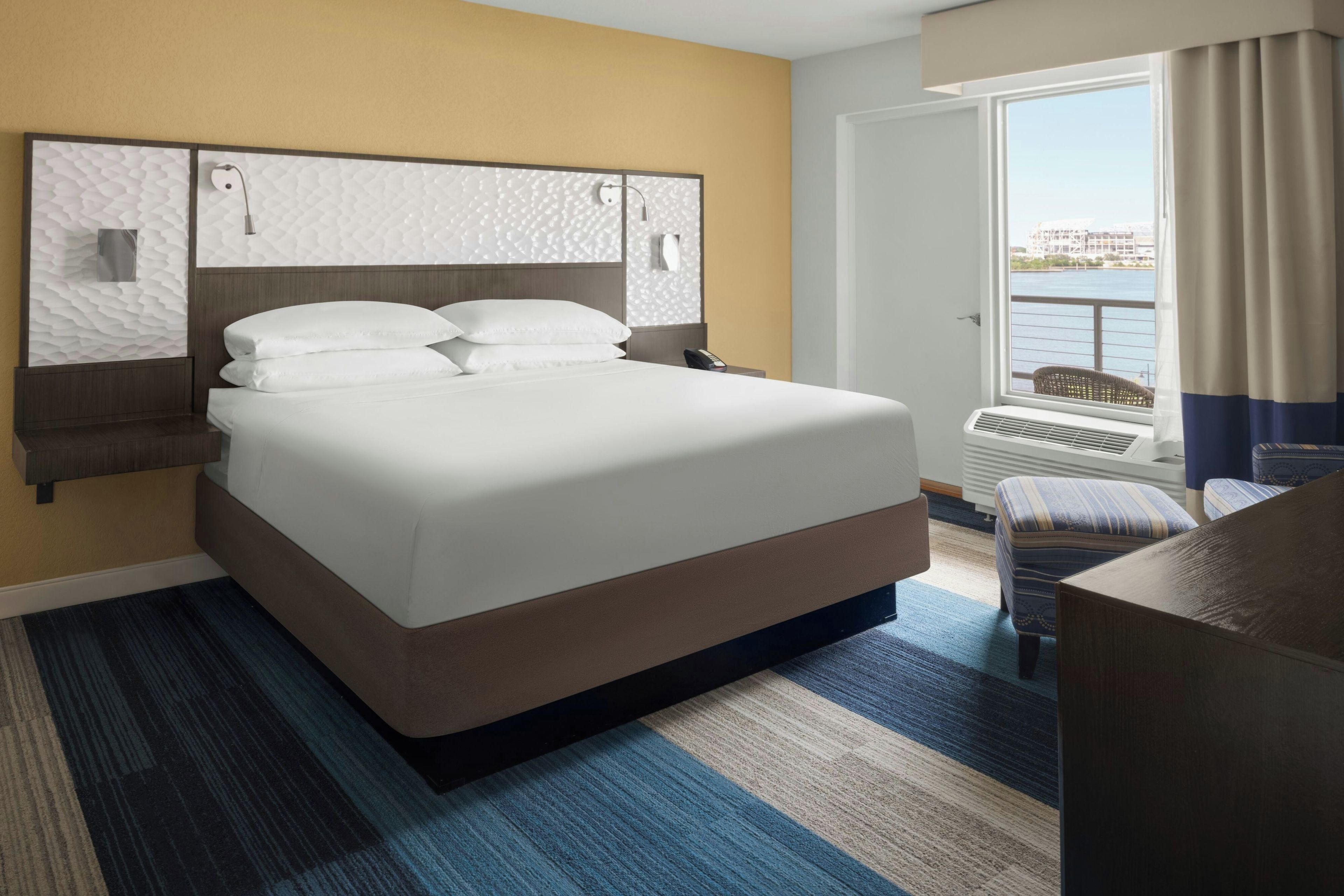 Een hotelkamer met een groot bed, een bureau, een stoel, een raam met uitzicht op het water en een deur.