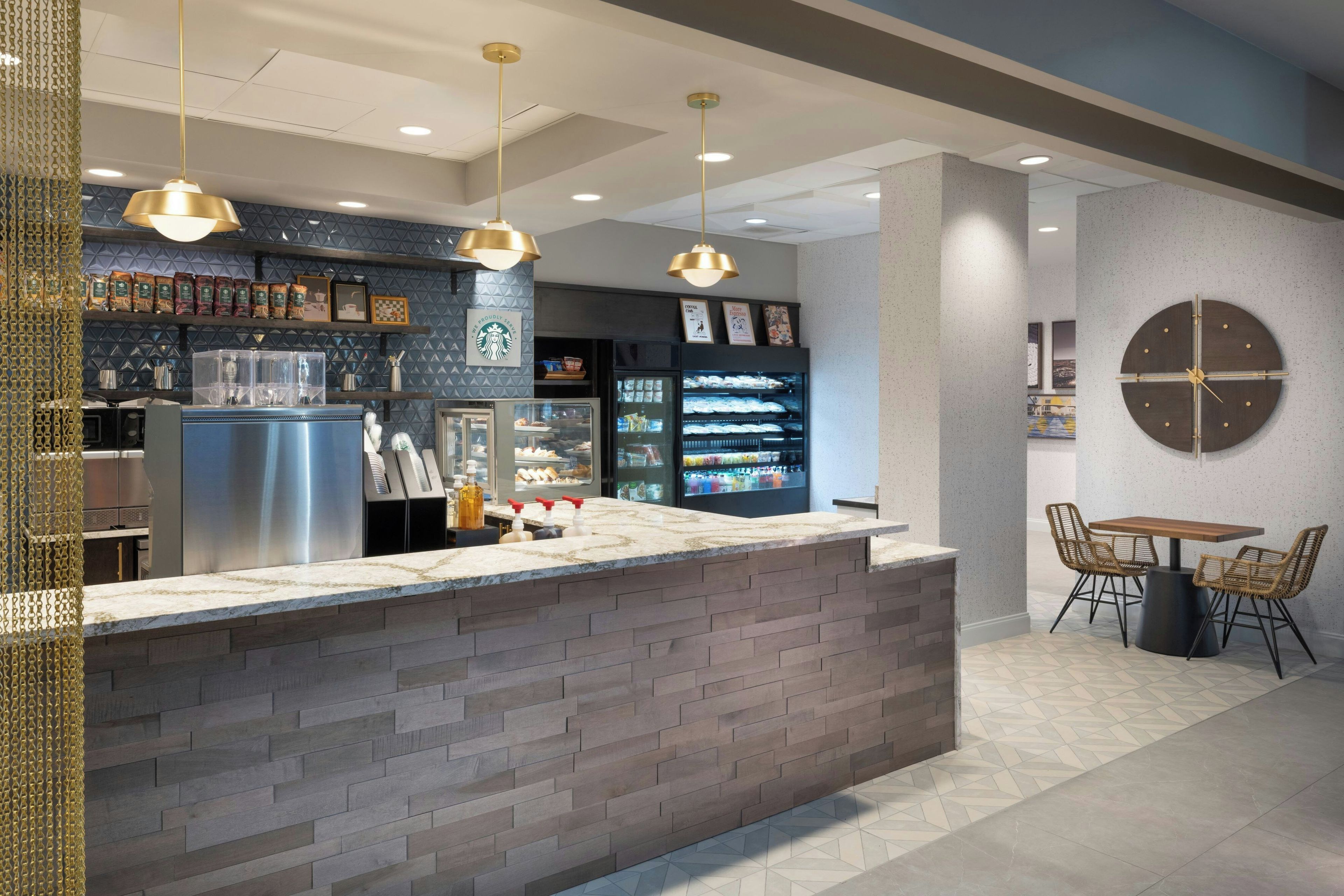 A modern cafe interior with a central island counter, seating area, and a clock on the wall.