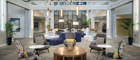 A spacious lobby with a central seating area, a staircase, and a high ceiling with modern lighting fixtures.