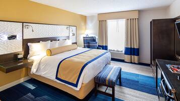 A hotel room with a large bed, a desk, a chair, a TV, and a window with curtains.