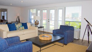 A living room with a sofa, armchairs, a coffee table, and a lamp. There is a window with blinds and a view of buildings outside. - Southbank Hotel by Marriott Jacksonville Riverwalk (Jacksonville)