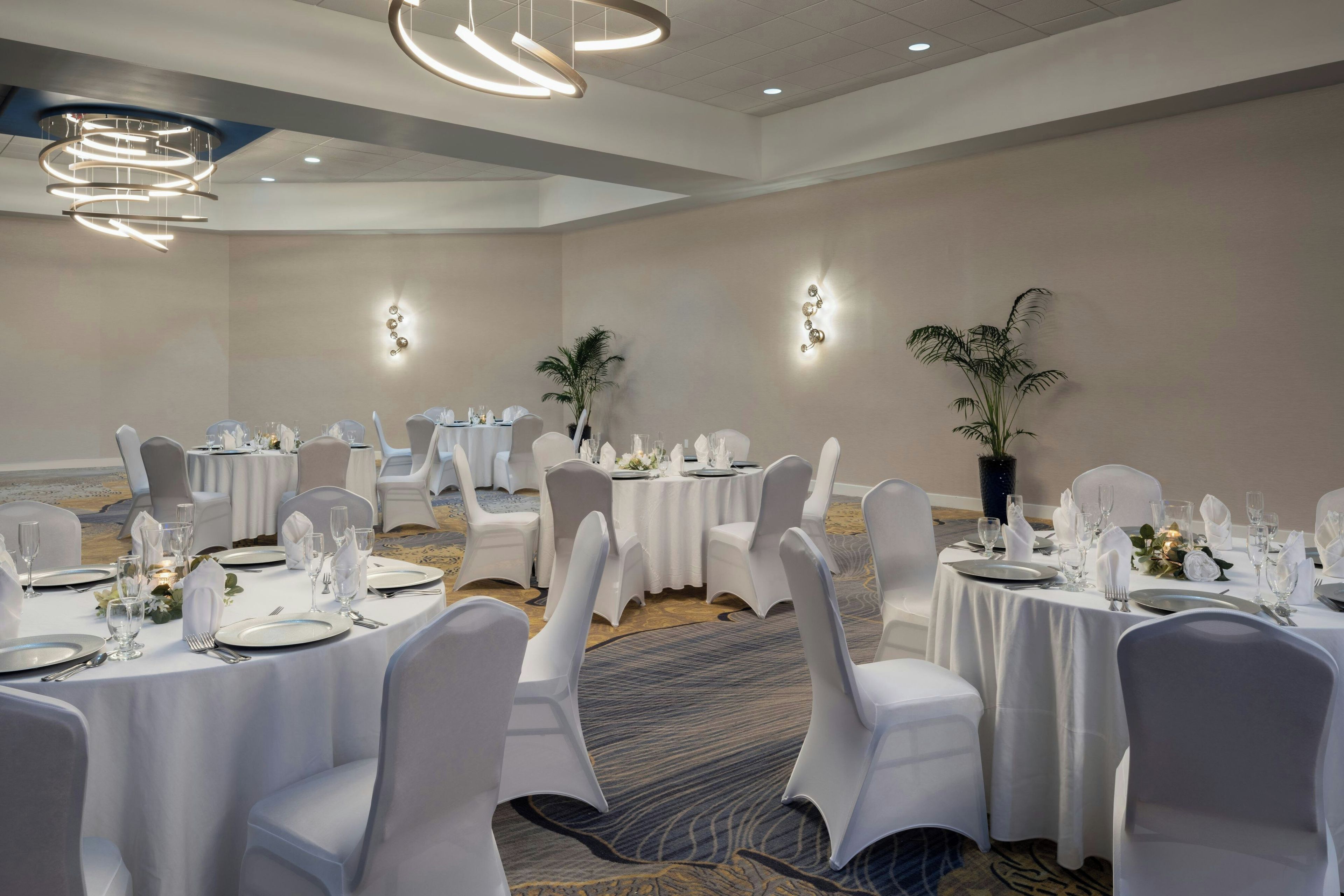 Un salón de banquetes con mesas redondas, manteles blancos y sillas.