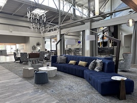 Un amplio espacio de sala con un sofá modular azul, alfombra estampada y lámparas modernas.