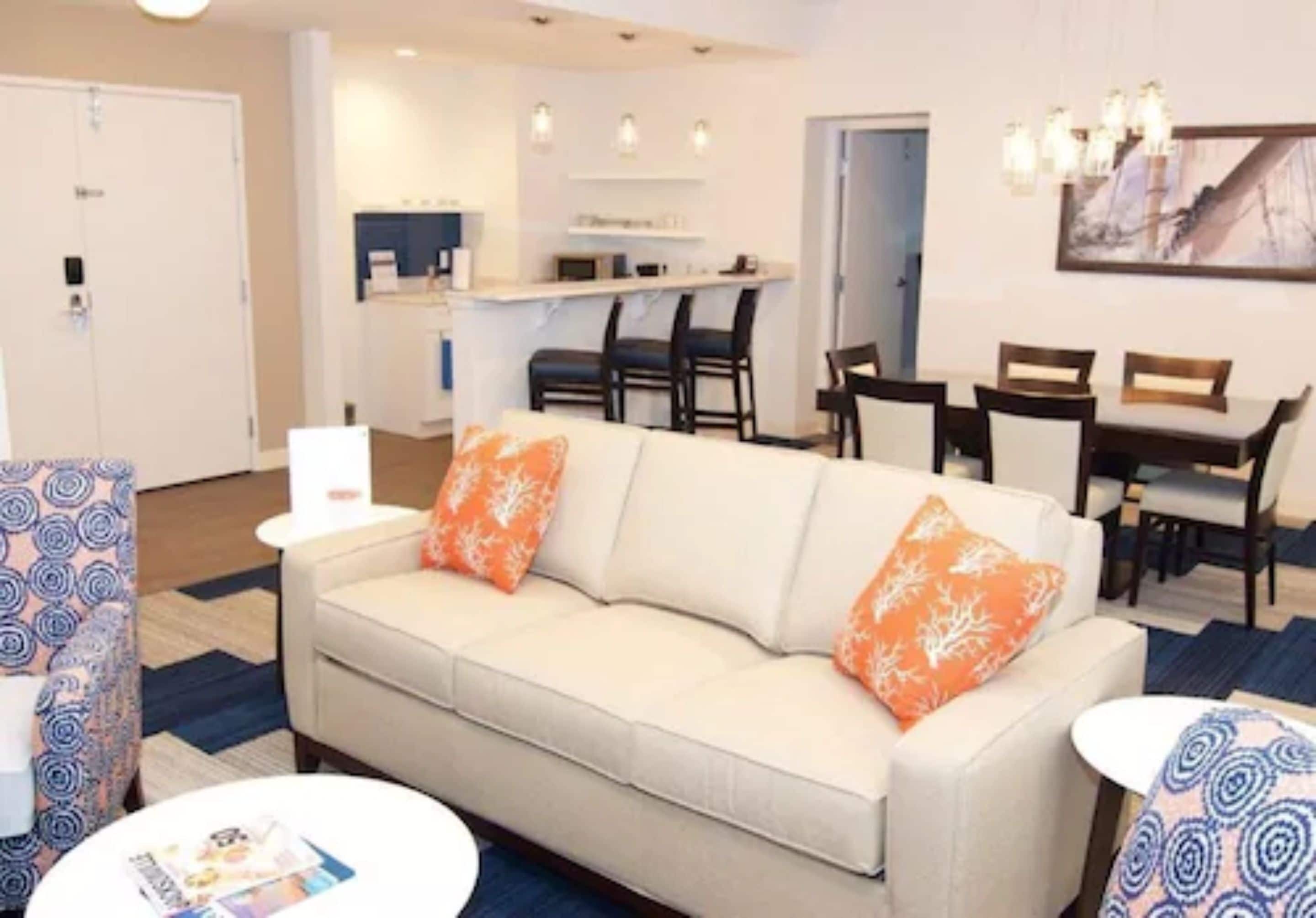 A modern living room with a sofa, chairs, a dining table, and a kitchen area in the background.