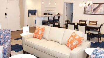 A modern living room with a sofa, chairs, a dining table, and a kitchen area in the background.