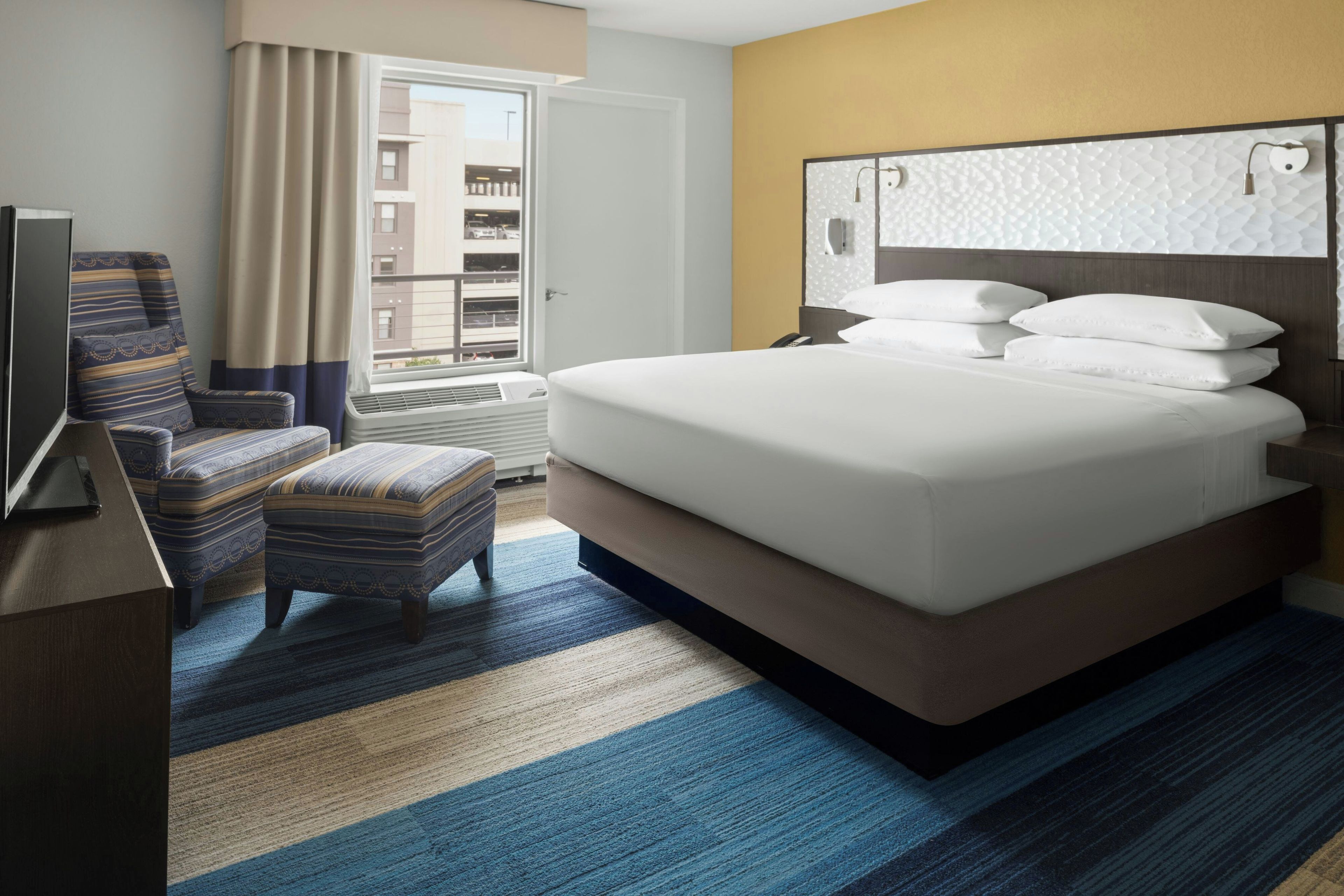 Una habitación de hotel con una cama, una silla, un escritorio y una ventana.