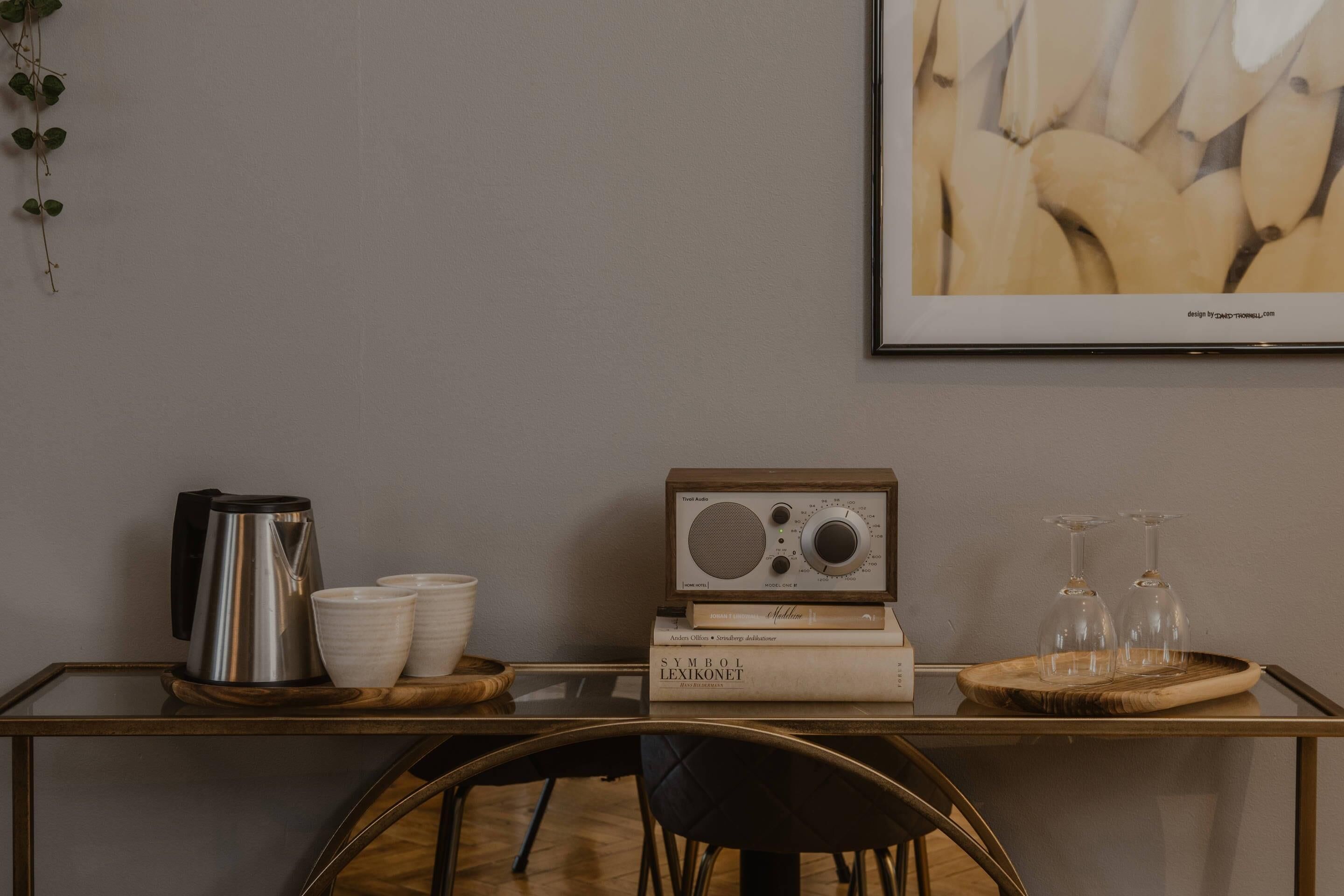A modern room with a glass table displaying a radio, books, and a tray with glasses.