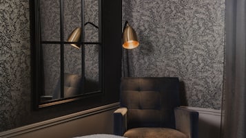A room with a patterned wallpaper, a dark armchair, and a floor lamp.