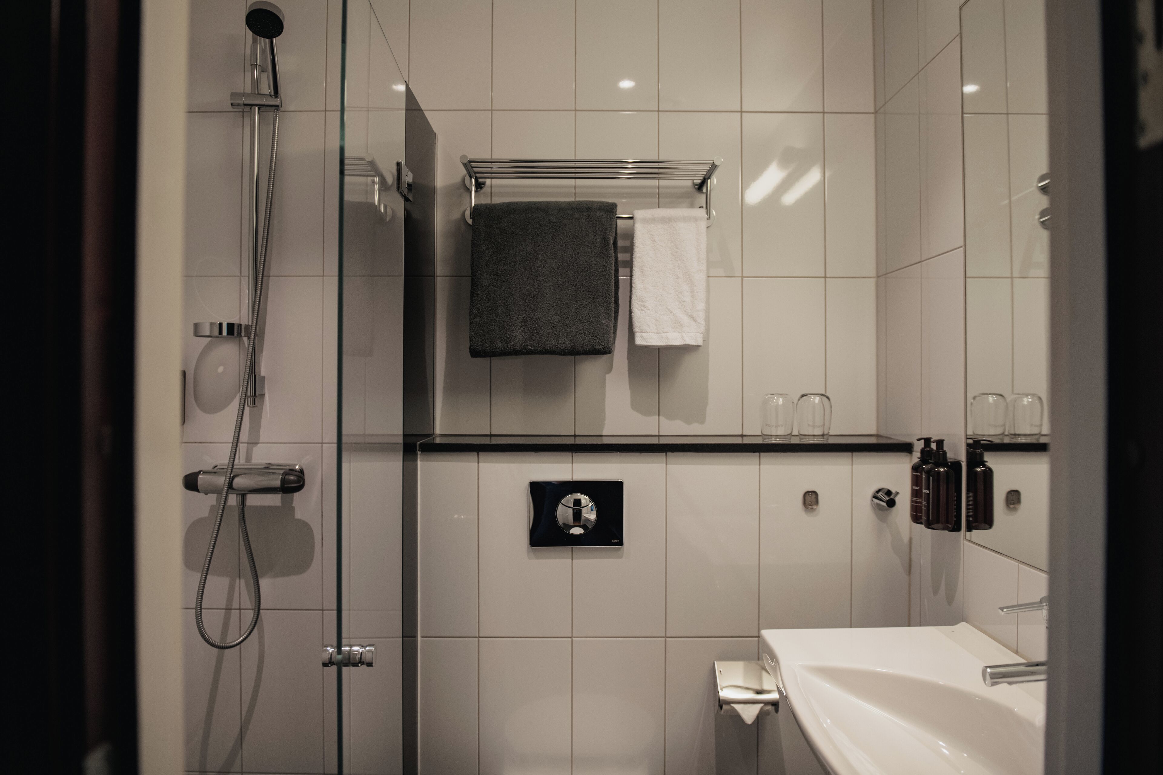 A modern bathroom with a glass shower enclosure, a white sink, and a towel rack with two towels.