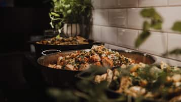 A kitchen with two large pans of food, a plant, and a tiled backsplash.